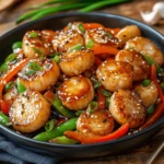 A beautifully plated fishcakes and scallops stir fry with golden-brown fishcakes, seared scallops, and colorful vegetables coated in a glossy sauce.